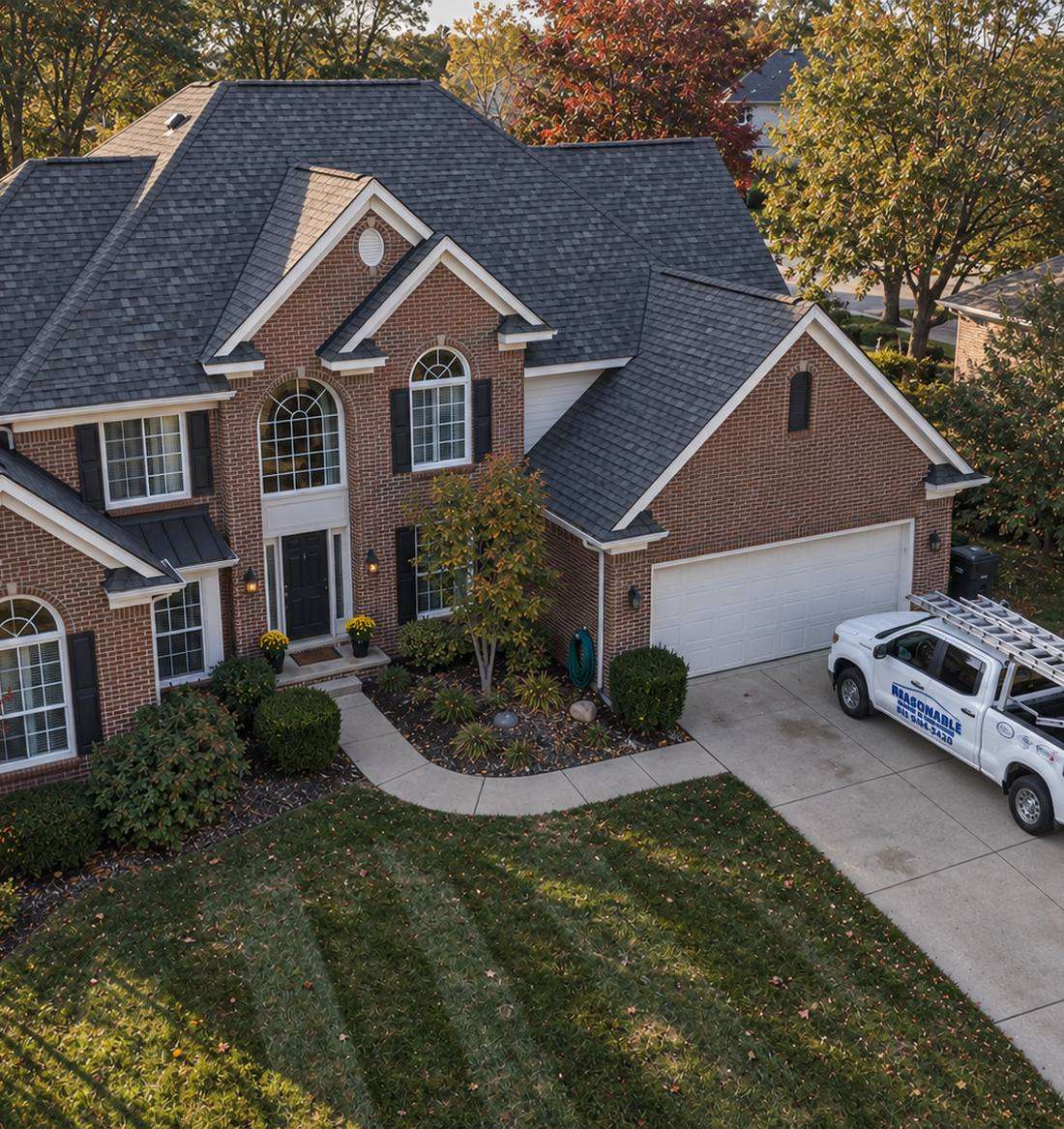 Aerial view of a completed Reasonable Roofing shingle roof on a Michigan brick colonial with the company truck in the driveway