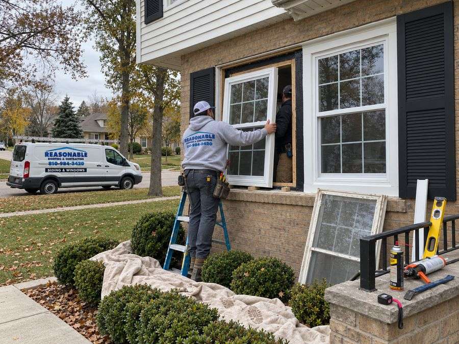 Reasonable Roofing crew fitting a replacement window on a Michigan brick home